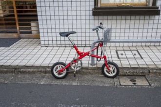 Small red folding bike with basket attached to railing