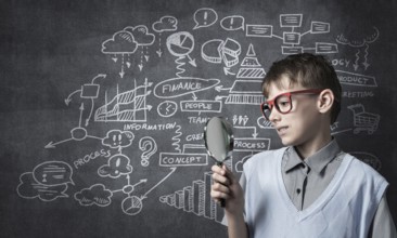Cute boy looking through magnifying glass against blackboard background