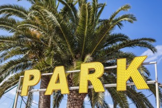 Entrance to an amusement park with big yellow lights sign and palm trees with bright blue sky on