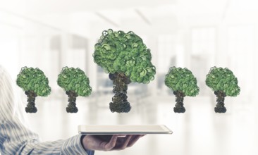 Close of businessman holding tablet pc with green tree made of gears and cogwheels. Mixed media