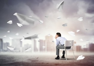 Young businessman sits on an office chair, thoughtful and looking up