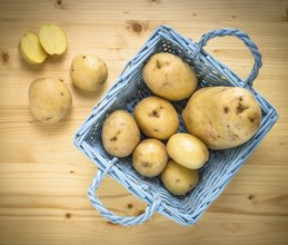 Fresh potatoes in wooden vintage basket on old table as background. Top view