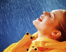A woman joyfully embracing the rain in a yellow raincoat, expressing freedom and happiness