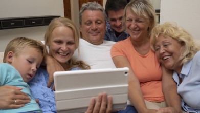 A big family is watching something funny on a pad, close side by side