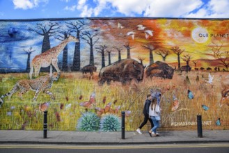 People passing by the graffiti wall art at Brick Lane Market in London, United Kingdom