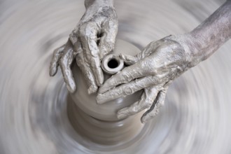 Pottery, artist muddy hands making clay pot giving shape on spinning wheel, semi urban village
