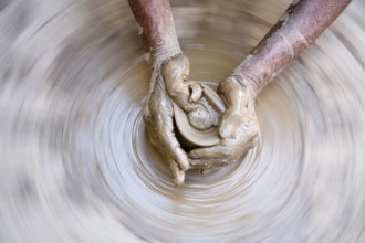 Pottery, artist muddy hands making clay pot giving shape on spinning wheel, semi urban village