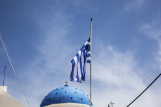 Greek flag waving in the wind, blue church dome, Timios Stavros church, Perissa, Santorini island,