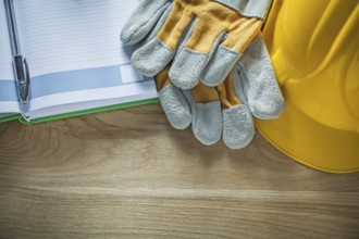 Protective gloves notepad pen safety hard hat on wooden board