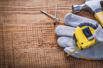Tapeline glove hammer nails on vintage wooden board with copyspace construction concept