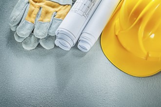 Rolled blueprints hard hat safety gloves on concrete background