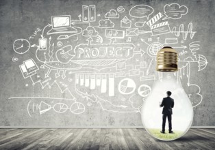 Businessman inside of light bulb in empty concrete room and sketches on wall