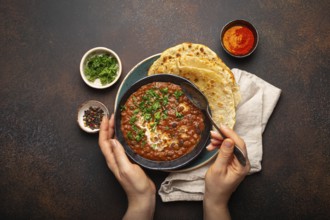 Female hands holding a bowl and eating traditional Indian Punjabi dish Dal makhani with lentils and