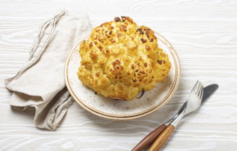 Whole roasted head of cauliflower with olive oil on plate on white wooden rustic table top view