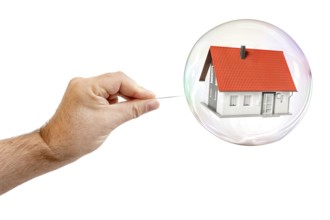 An image of a soap bubble with a house and a males hand with needle to let the dream pop
