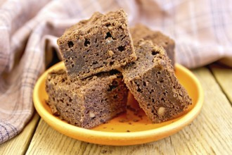 Piece of chocolate cake in a clay plate, napkin on a wooden boards background