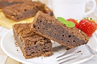 Two pieces of chocolate cake on a plate with strawberries and mint on a fork against a linen