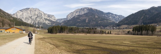 Cyclist on the Lamingtal cycle path between farmland in spring, Pribitz mountain and Meßnerin
