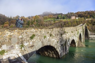 Elderly tourist photographs a magnificent landscape. Ponte della Maddalena Bridge. Cold green
