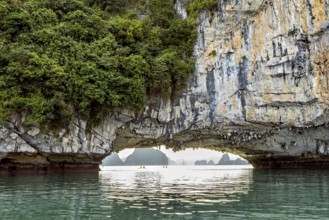 Natural scenery with rock formation over calm water, rock bridge and cave in Halong Bay in Vietnam