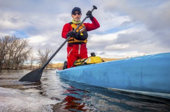 Senior paddler in a dry suit and life jacket is training on stand up paddleboard on a mountain lake