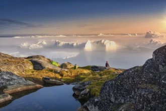 Large glaciers in the bay by the rocky shore in the light of the setting sun with fog over the