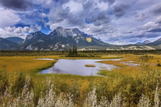 Cloudy Indian summer in the Rockies of Canada. Rocks, lakes and yellow grass under flying clouds.