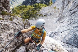 Caucasian woman mountaineer climbing up the mountain on via ferrata trail, high up in the mountain