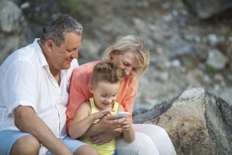 Happy grandparents and grandson with smartphone outdoor. Grandmother and grandfather watching the