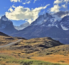 The gravel road is bent between yellowed hills and go to the snow-covered rocky mountains. Midday