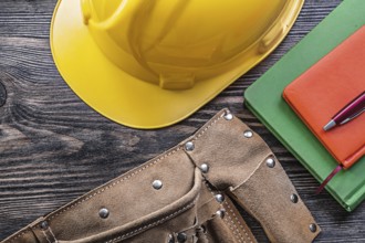 Tool belt note-books pen building helmet on wooden board construction concept