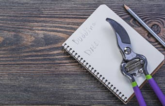 Notepad pencil secateurs on vintage wooden board gardening concept