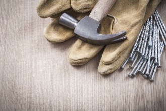 Claw hammer leather protective gloves and heap of metal nails on wooden board close up version