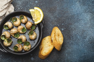 Escargots de Bourgogne Snails with Garlic Butter and Parsley in black cast iron pan with Lemon and
