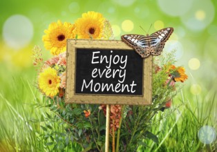 An image of a little chalkboard in the garden with the message Enjoy every Moment