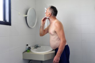 Man 60 plus shaves wet in the bathroom