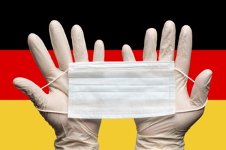 Doctor holding medical face mask in two hands in white gloves on background flag of Germany.