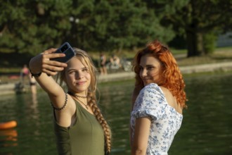 Two close friends take a joyful selfie by a serene and beautiful lake, capturing the essence of
