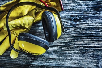 Safety earmuffs leather gloves on wooden board