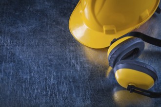 Noise insulation ear muffs and hard hat on scratched metallic background copy space image