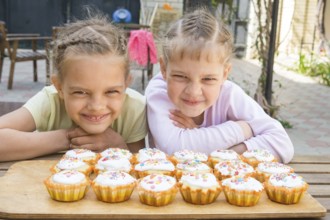 Two girls pretending funny faces, sitting in front of easter cupcakes