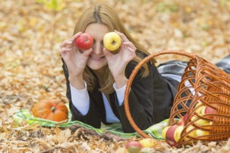 Young beautiful girl lying on the leaves in the autumn forest in the fun and put the apples to the