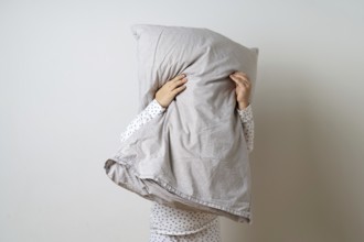 Portrait of pretty caucasian girl in white pyjama and pillow in studio white background .