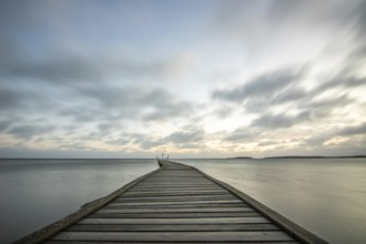 Sunrise over a lake in autumn. A wooden jetty juts into the water, while grass has established