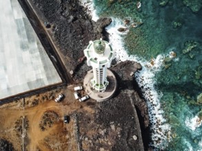 Aerial top view of lighthouse, rocks and ocean waves in a volcanic landscape with lava. Punta Lava