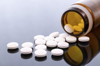 White pills and brown glass bottle isolated on black reflective surface. Global pharmaceutical