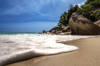 Waves crash over a peaceful tropical beach lined with rocks and trees, La Digue, Seychelles