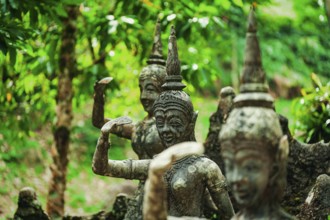 Weathered stone statues amidst green foliage in a forest setting, figures, stone figures,