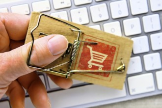Hand in mousetrap with shopping trolley in front of a computer keyboard, photomontage