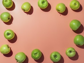 Green apples on orange or coral pink background with copy space for text or design in center,
